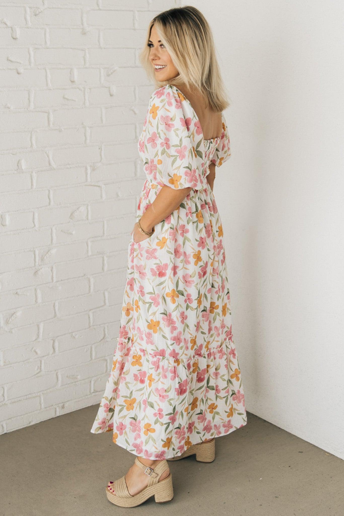 Blonde woman wearing a floral print maxi dress with square neckline and puffed half length sleeves.