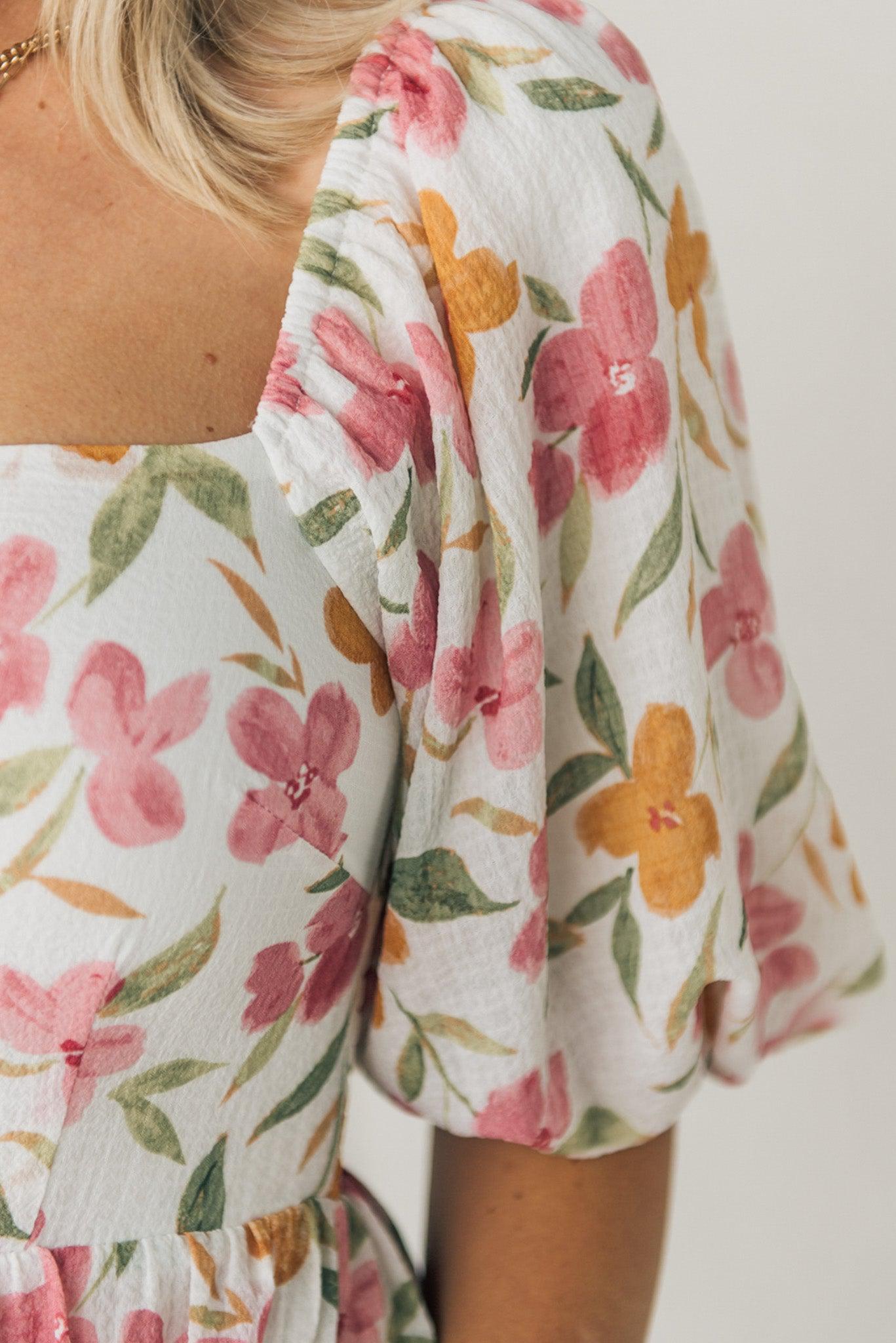 Blonde woman wearing a floral print maxi dress with square neckline and puffed half length sleeves.