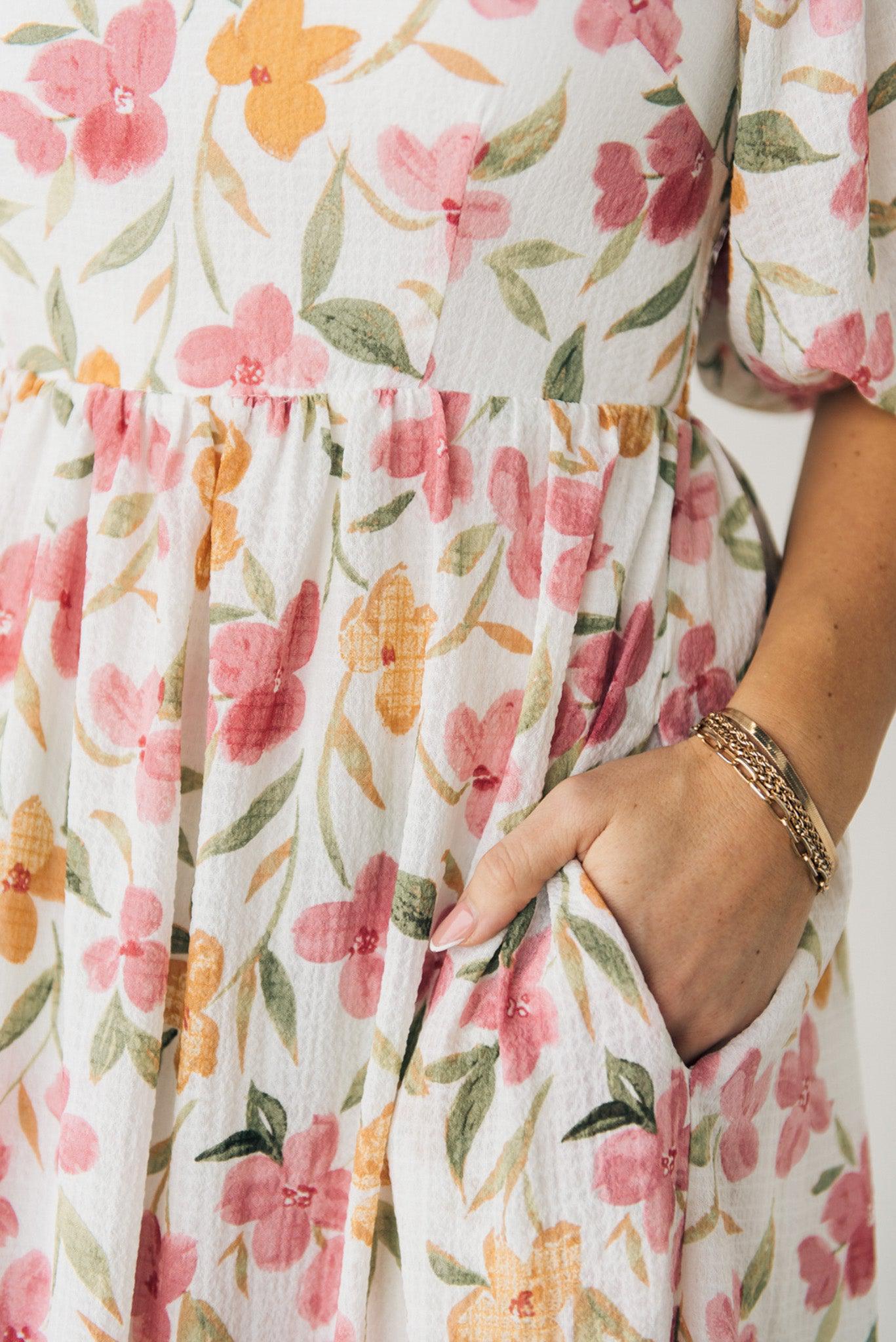 Blonde woman wearing a floral print maxi dress with square neckline and puffed half length sleeves.