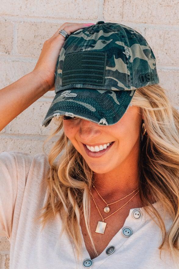 Blonde woman wearing a single color distressed american flag hat.