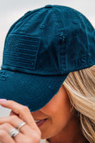 Blonde woman wearing a single color distressed american flag hat.