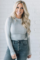 A woman wearing a solid, ribbed, slim fit sweater with a round neck, long sleeves, and tucking it into high-waisted jeans.