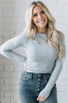 A woman wearing a solid, ribbed, slim fit sweater with a round neck, long sleeves, and tucking it into high-waisted jeans.