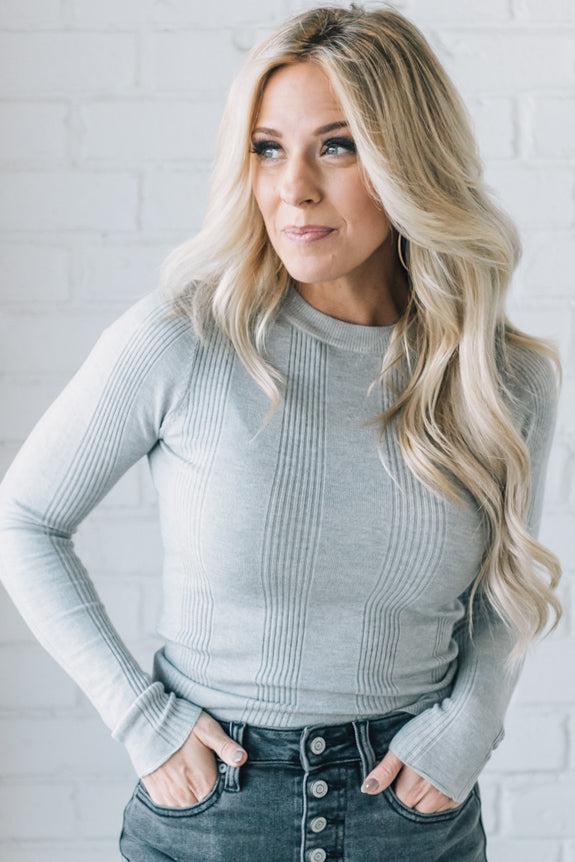 A woman wearing a solid, ribbed, slim fit sweater with a round neck, long sleeves, and tucking it into high-waisted jeans.