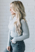 A woman wearing a solid, ribbed, slim fit sweater with a round neck, long sleeves, and tucking it into high-waisted jeans.