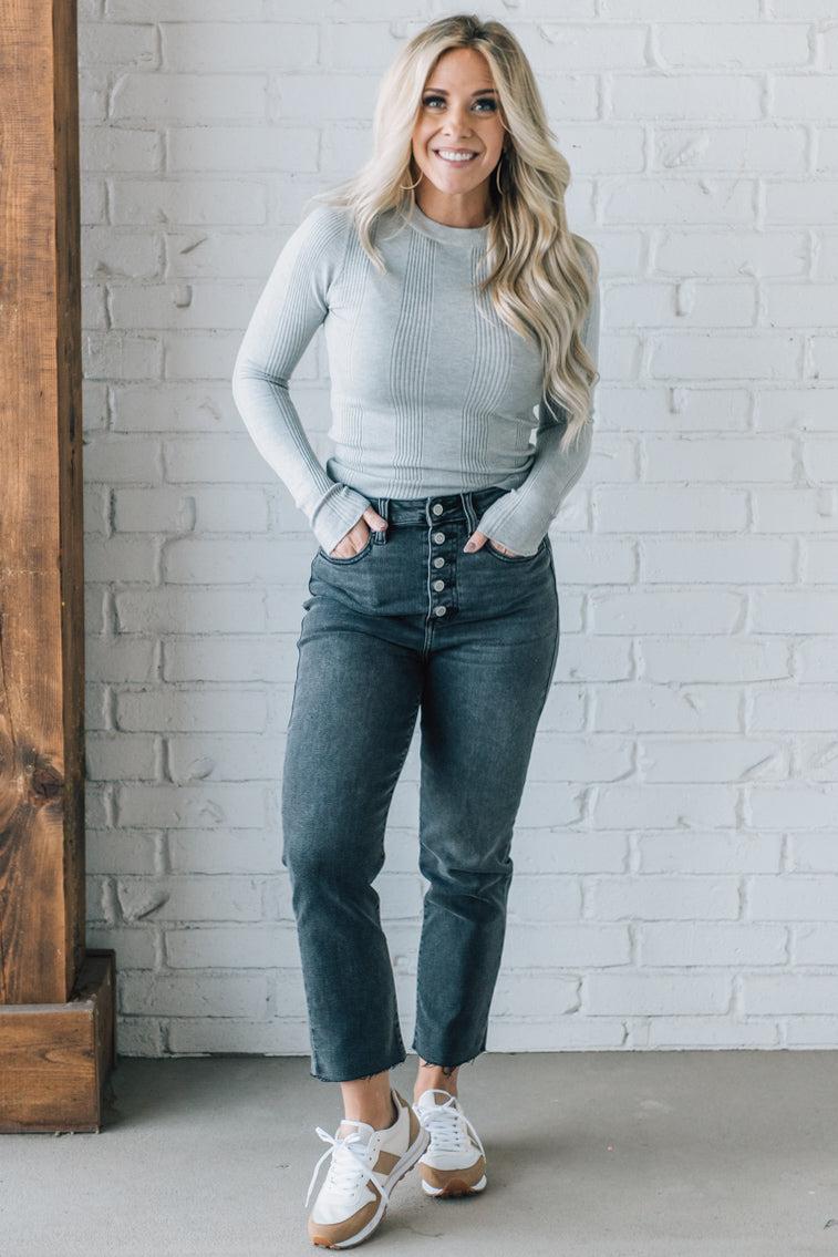 A woman wearing a solid, ribbed, slim fit sweater with a round neck, long sleeves, and tucking it into high-waisted jeans.