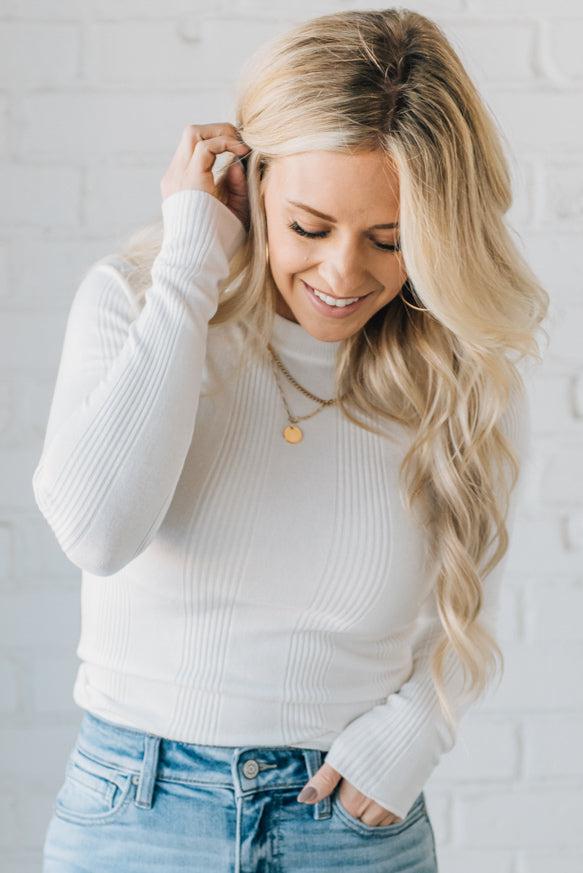 A woman wearing a solid, ribbed, slim fit sweater with a round neck, long sleeves, and tucking it into high-waisted jeans.