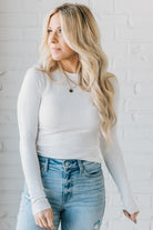 A woman wearing a solid, ribbed, slim fit sweater with a round neck, long sleeves, and tucking it into high-waisted jeans.