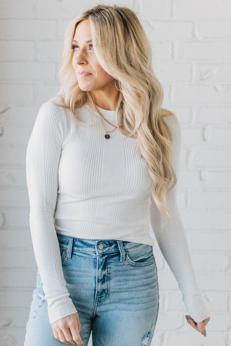 A woman wearing a solid, ribbed, slim fit sweater with a round neck, long sleeves, and tucking it into high-waisted jeans.