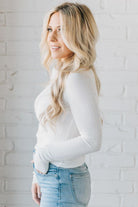 A woman wearing a solid, ribbed, slim fit sweater with a round neck, long sleeves, and tucking it into high-waisted jeans.