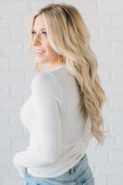 A woman wearing a solid, ribbed, slim fit sweater with a round neck, long sleeves, and tucking it into high-waisted jeans.