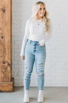 A woman wearing a solid, ribbed, slim fit sweater with a round neck, long sleeves, and tucking it into high-waisted jeans.