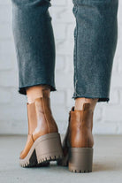 BROWN LEATHER BOOTS WITH BLACK CROP JEANS AGAINST A WHITE BRICK WALL.