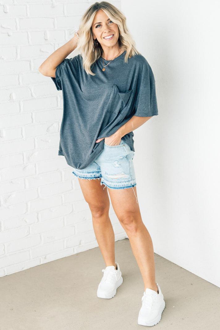 Blonde woman wearing an oversized solid tee with front pocket, and raw scissor cut edges.