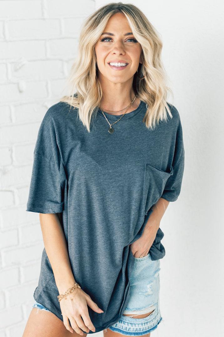 Blonde woman wearing an oversized solid tee with front pocket, and raw scissor cut edges.