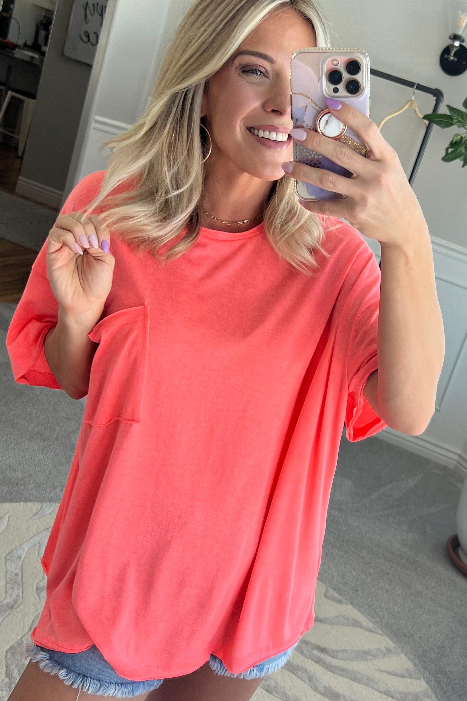 Blonde woman wearing an oversized solid tee with front pocket, and raw scissor cut edges.