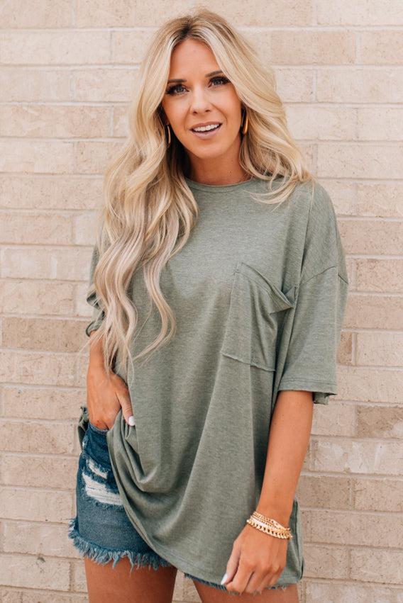 Blonde woman wearing an oversized solid tee with front pocket, and raw scissor cut edges.
