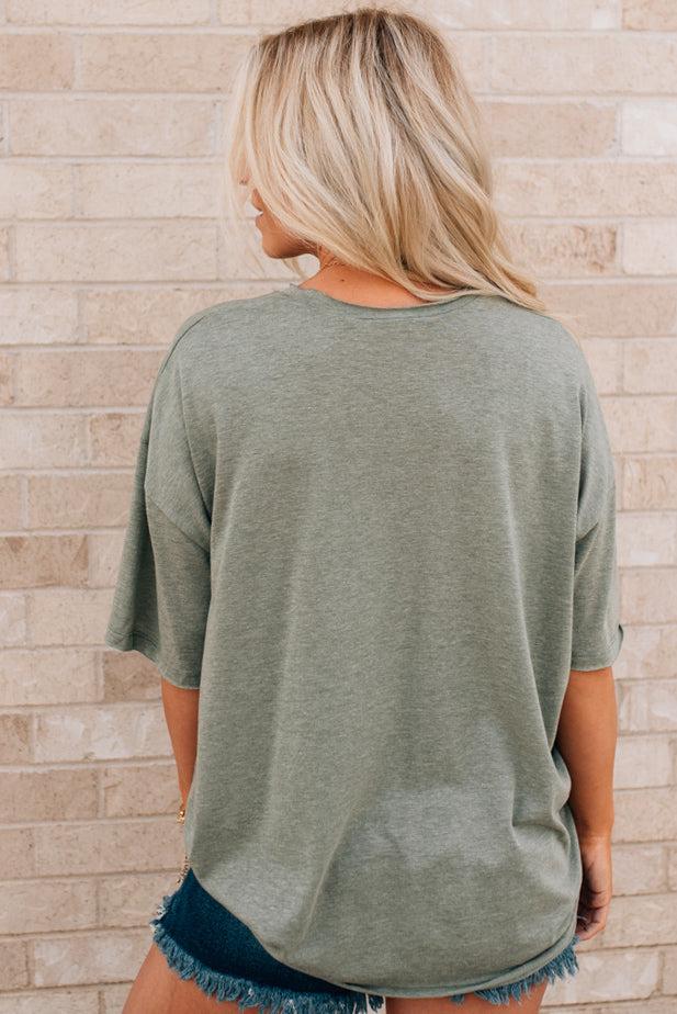 Blonde woman wearing an oversized solid tee with front pocket, and raw scissor cut edges.
