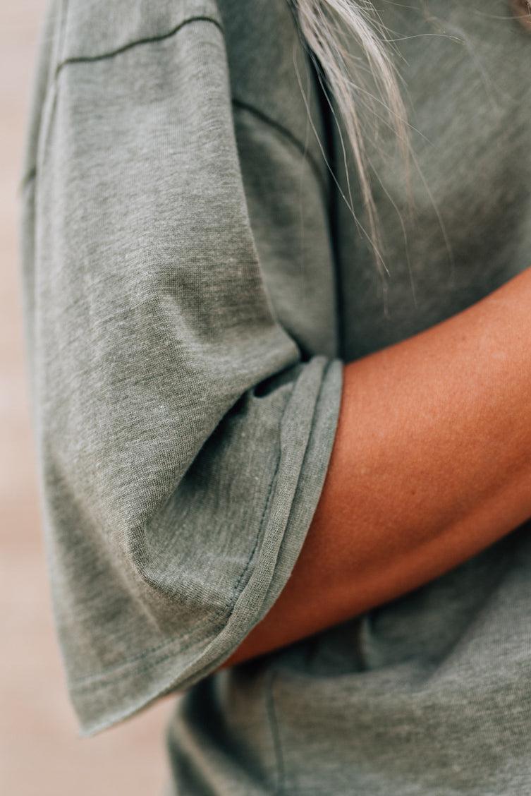 Blonde woman wearing an oversized solid tee with front pocket, and raw scissor cut edges.