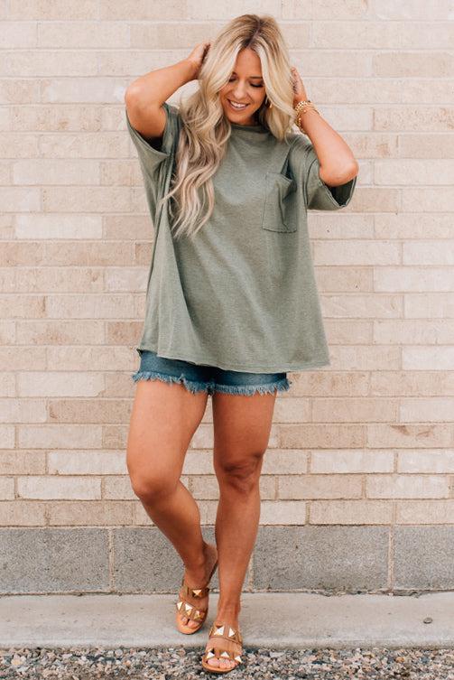 Blonde woman wearing an oversized solid tee with front pocket, and raw scissor cut edges.