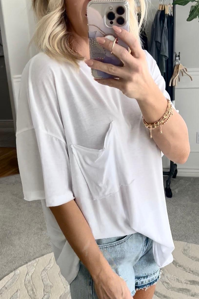 Blonde woman wearing an oversized solid tee with front pocket, and raw scissor cut edges.