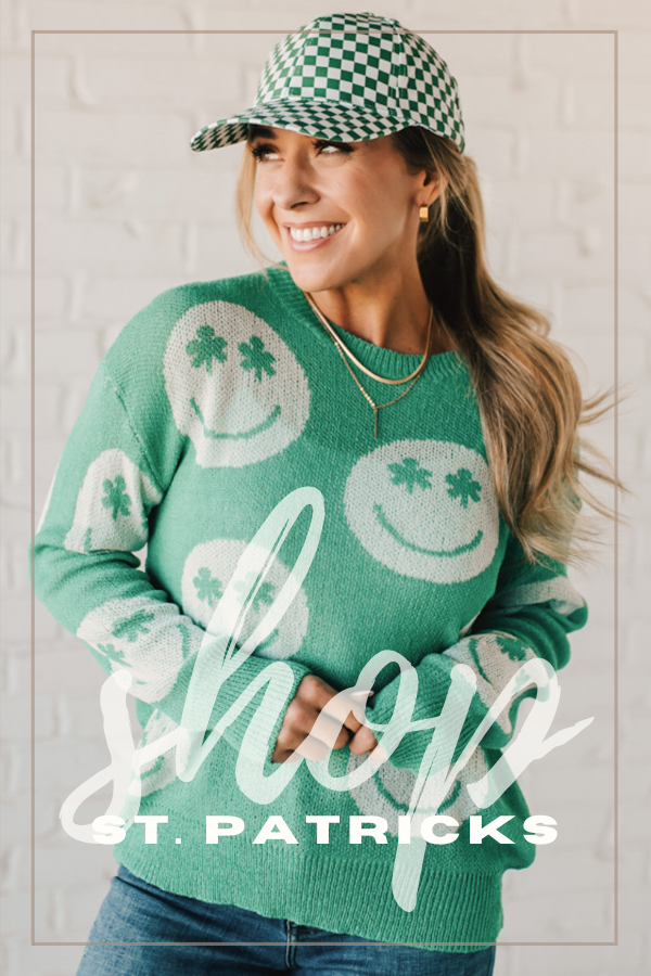 Blonde woman modeling a lightweight green long sleeve sweater with big white smiley faces thoughout