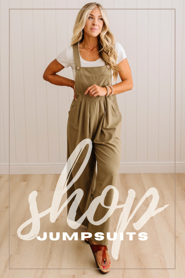 A woman modeling an olive green jumpsuit over a white t-shirt, standing in front of a white paneled wall and light wood floor. A large white text overlay at the bottom reads 'shop JUMPSUITS'.