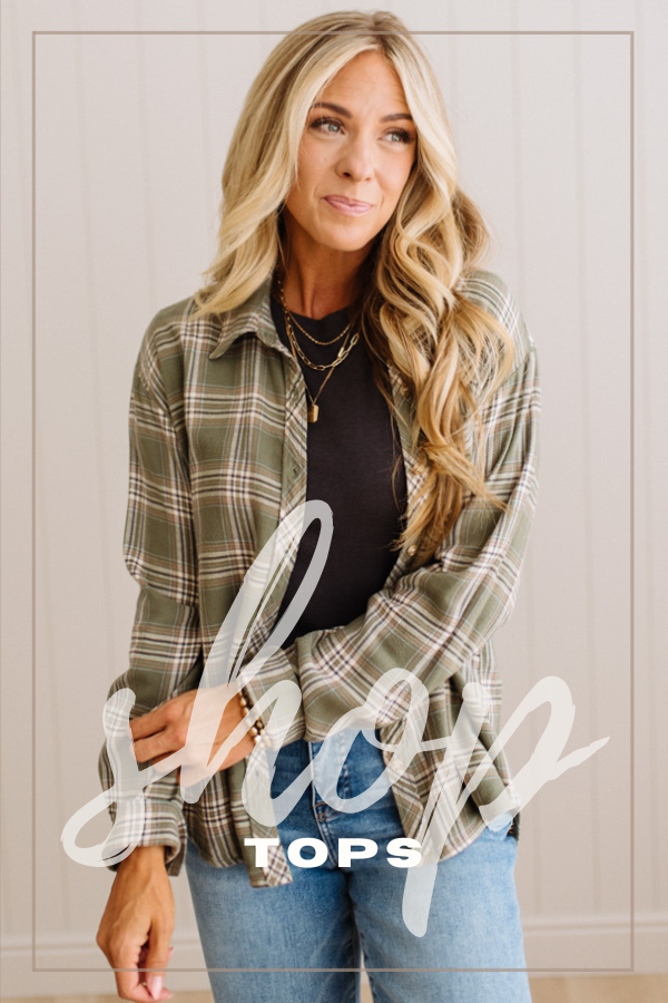 A woman modeling a long-sleeve green plaid button-up shirt over a charcoal top and blue jeans, standing against a light paneled wall. A large white script overlay reading 'shop' and smaller text 'TOPS' are across the lower portion of the image.