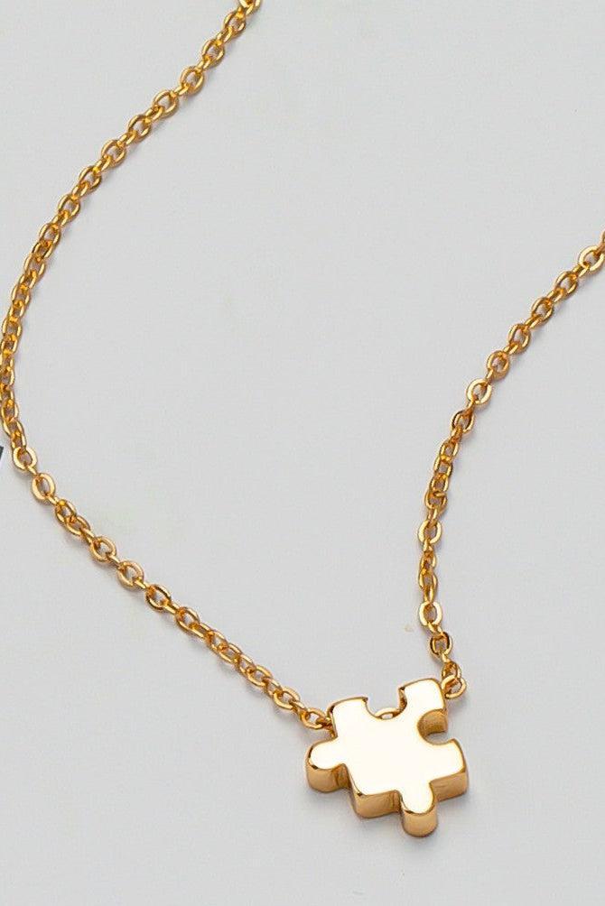 Gold necklace with a puzzle piece pendant on a light gray background