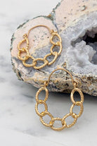 Gold chain earrings on a textured stone surface