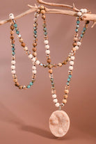 Necklace with beads and a large pendant on a branch against a brown background