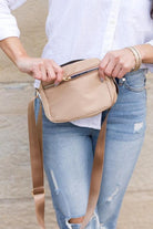 Person holding a beige crossbody bag with a blurred background