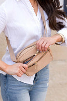 Person holding a beige crossbody bag with a blurred background