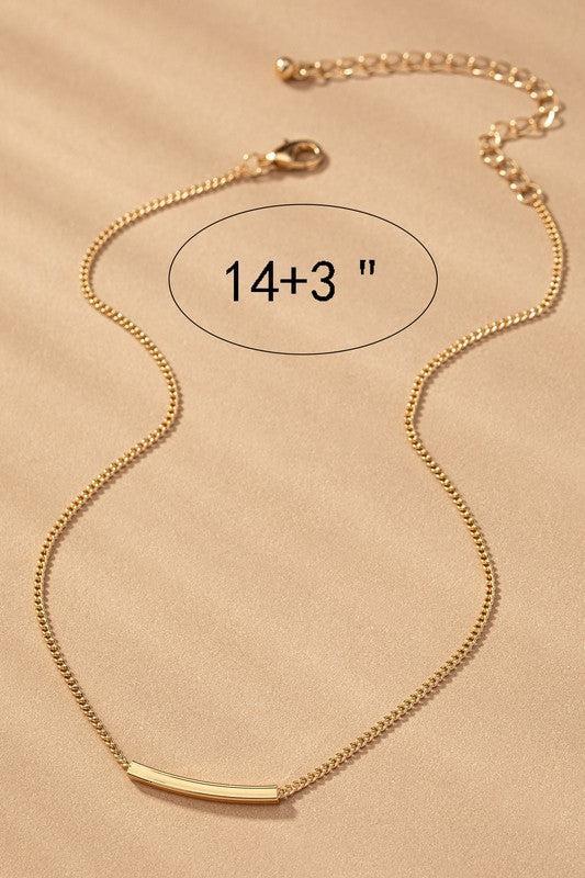 Gold necklace with a bar pendant on a beige background