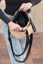 Blonde woman in black shirt wearing a tan crossbody bag with black zippers.