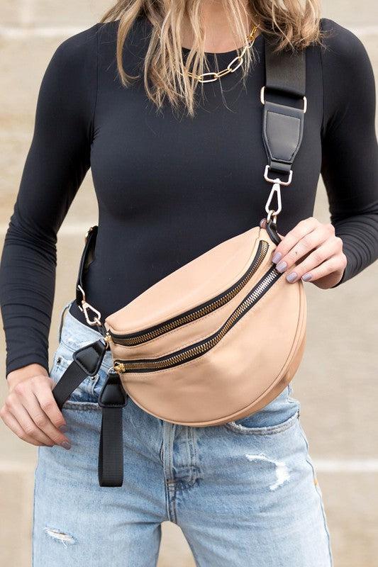 Blonde woman in black shirt wearing a tan crossbody bag with black zippers.