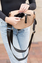 Blonde woman in black shirt wearing a tan crossbody bag with black zippers.