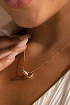 Close-up of a gold necklace with a pendant being worn.