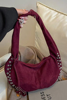 Maroon handbag with decorative studs held by a person against a neutral background