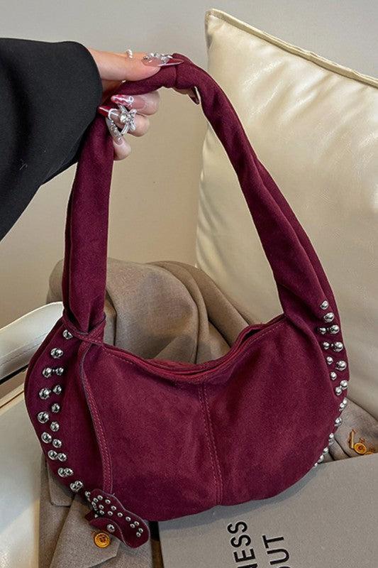 Maroon handbag with decorative studs held by a person against a neutral background