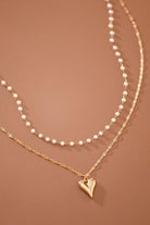 Two pearl necklaces with a gold heart pendant on a brown background