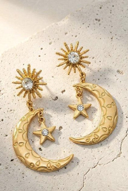 Gold earrings with moon, star, and sun designs on a textured beige surface