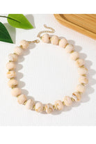 A close-up of a beaded strand with large round pale blush-beige stones separated by small metallic gold spacers, photographed on a white surface.