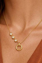 Gold necklace with circular pendant and three small crystals on a person's neck.