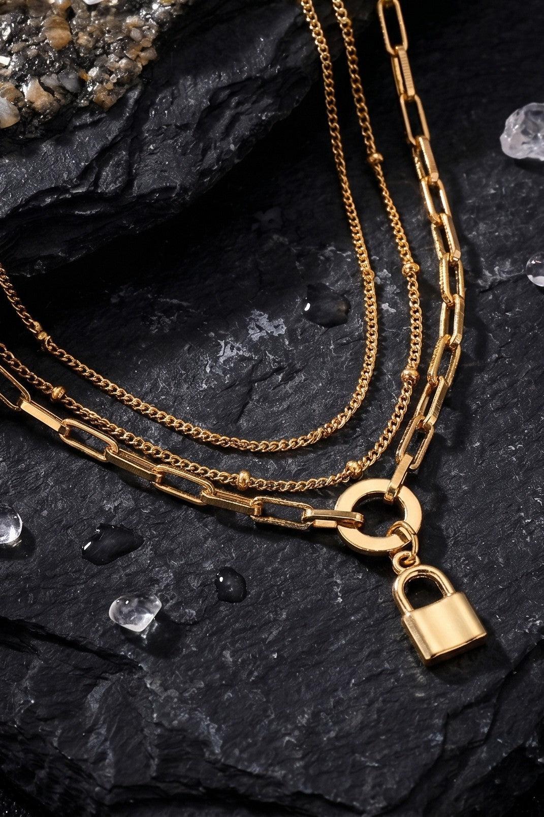Gold chain necklace with a lock charm on a dark stone surface