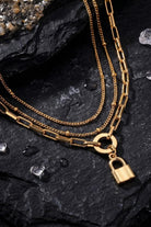 Gold chain necklace with a lock charm on a dark stone surface