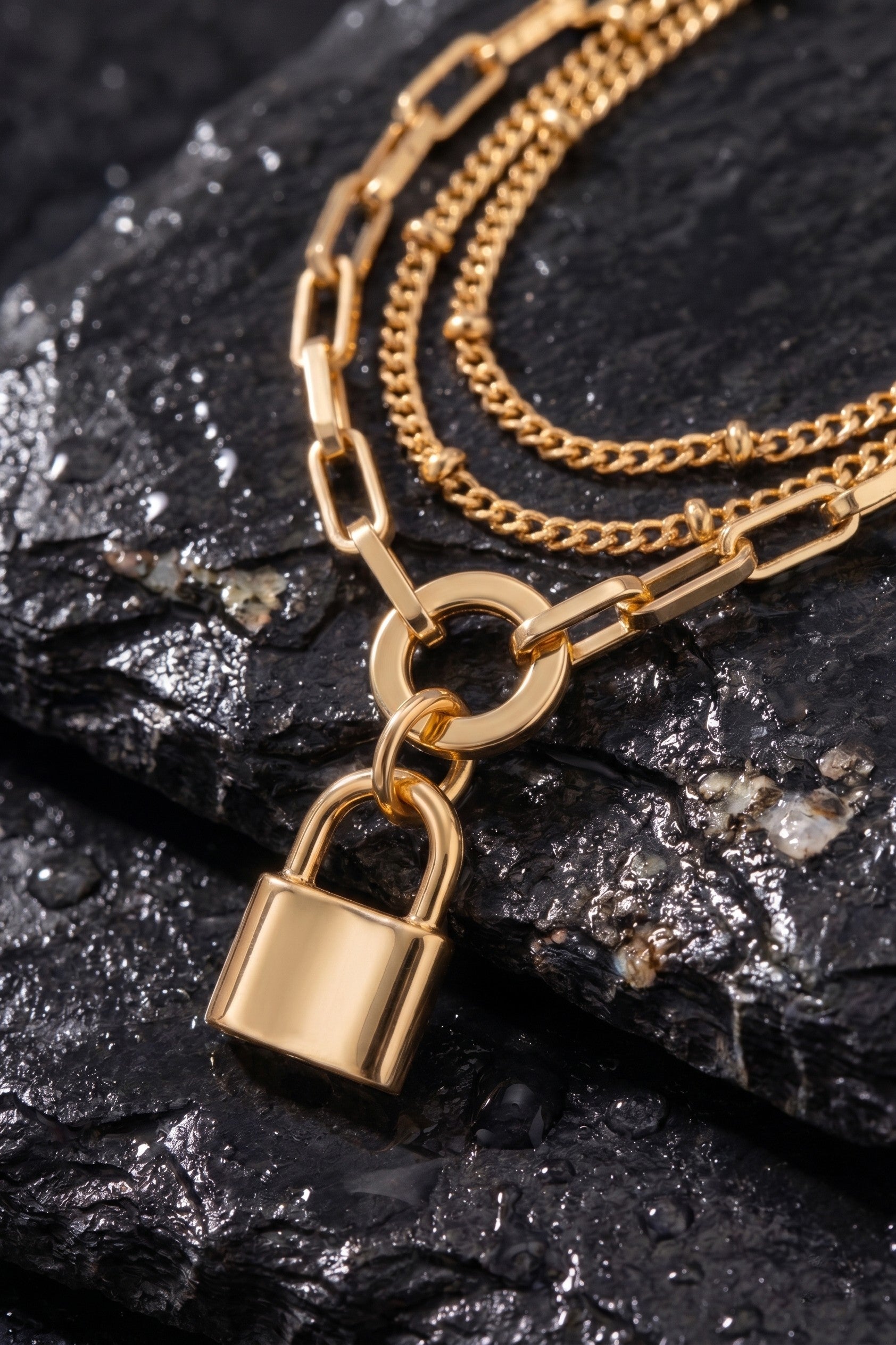 Gold chain necklace with a padlock charm on a dark stone surface