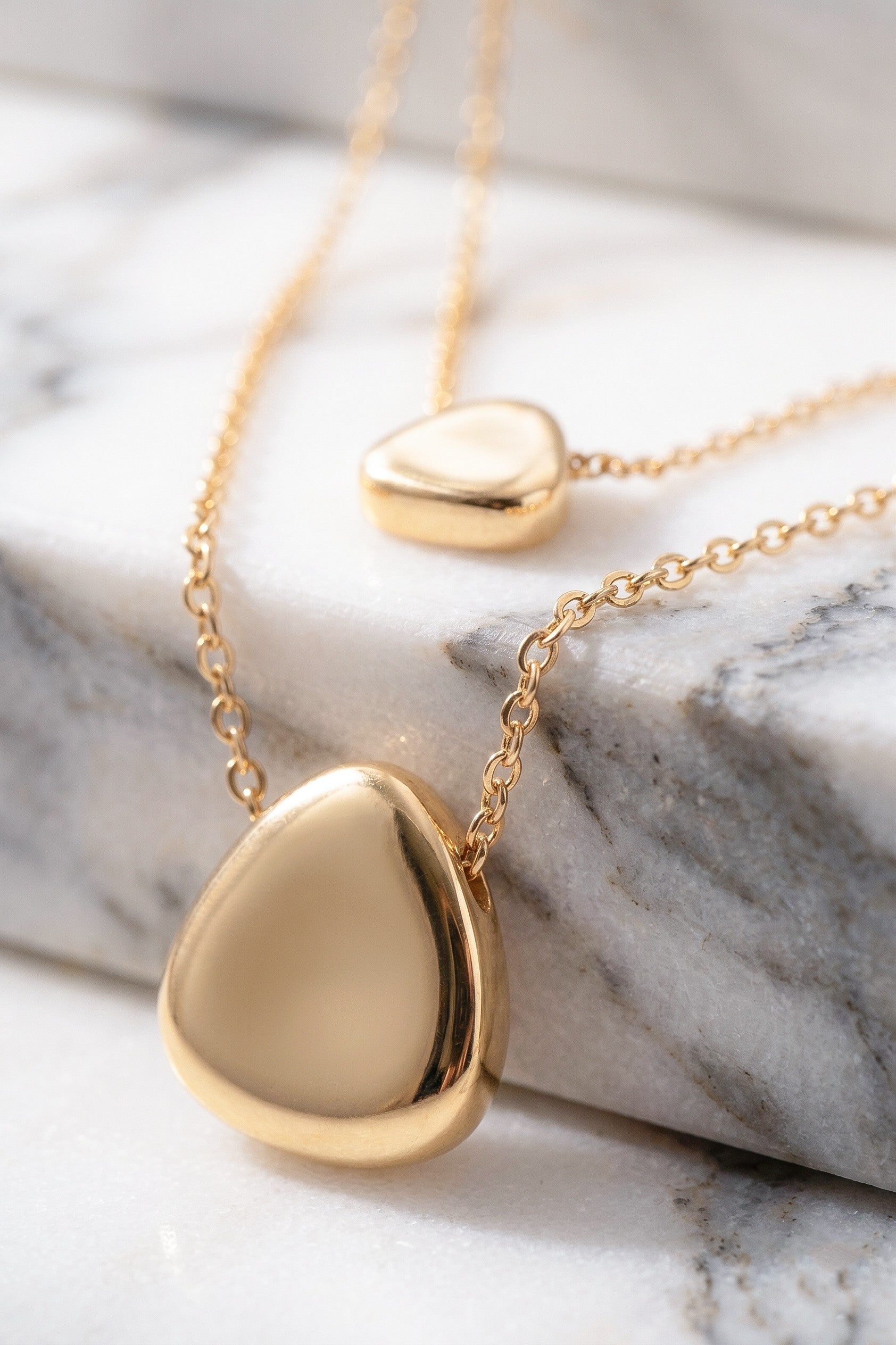 Gold necklaces with heart-shaped pendants on a marble surface