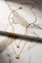 Two gold necklaces with heart pendants on a marble surface