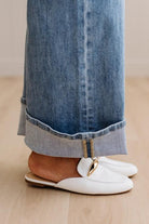 White loafers worn with rolled-up blue jeans on a wooden floor.